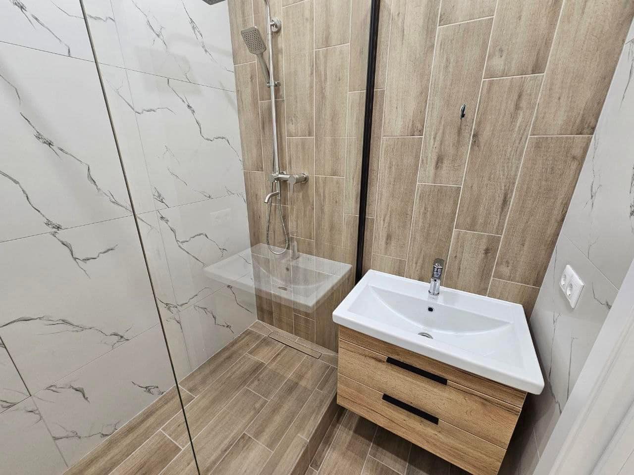 Kompaktne dušinurgaga valmis vannituba heleda plaadi ja puidutoonis detailidega